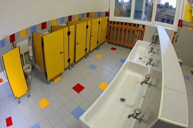 Düşük lavabolu ve çocuksuz sarı tuvaletli bir anaokulunun banyosu.