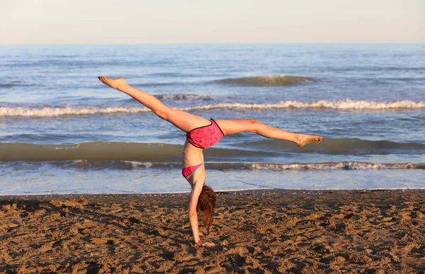 ビーチの岸に足を上げリズム体操をしている若い運動女の子 — ストック写真
