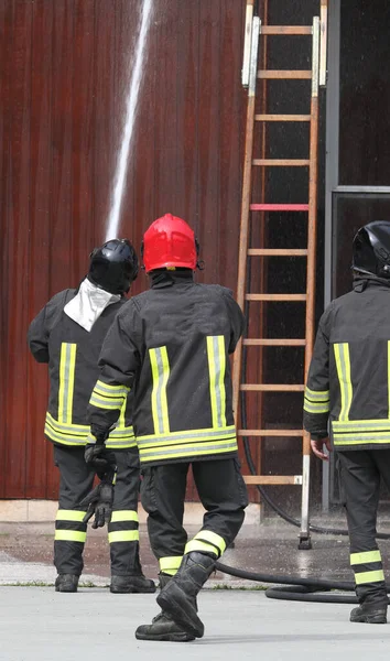 Tři Hasiči Akci Požárním Hydrantem Žebříkem Pozadí Při Výcviku Hasičské — Stock fotografie