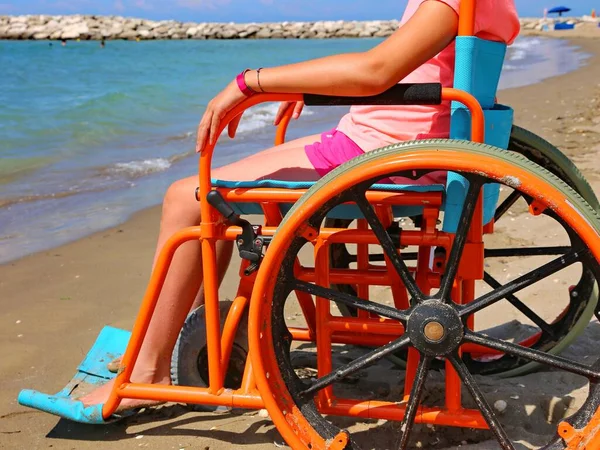 girl in a wheelchair with wheels modified to move on the sandy beach by the sea