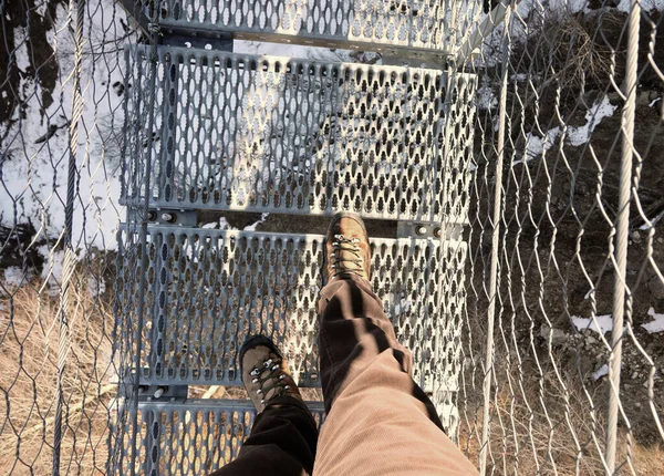 lightweight boots and legs of man on the spectacular suspension bridge made of steel ropes and metal sleepers