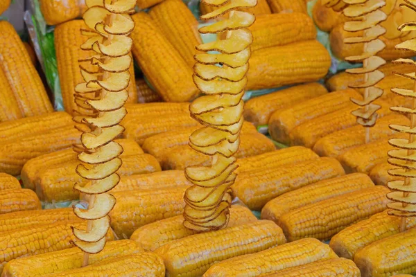 黄色の調理された有機トウモロコシの櫛通りの屋台で販売のためのプラスチック製のラップと長い揚げジャガイモ串 — ストック写真