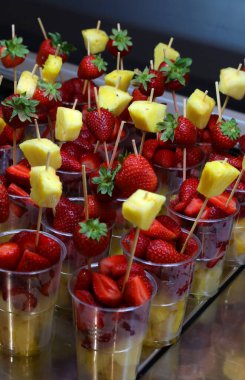 Yazın tropik sahil barında satılık bardakların içinde çilekli taze meyve ve ananas dilimleri.