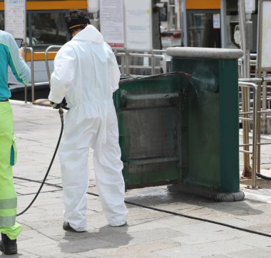 Haşere kontrol şirketinde koruyucu kıyafetle çalışan bir işçi. Virüsle mücadele etmek için güçlü bir su püskürtüsüyle sokak mobilyalarını temizlerken.