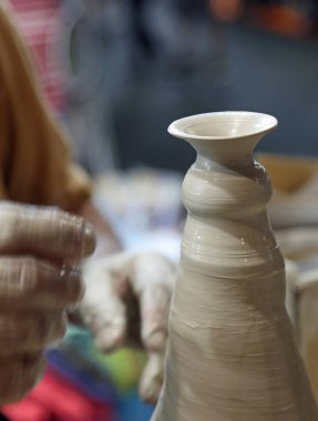 Yaşlı çömlekçi hassas parmaklarıyla malzeme üzerinde hafif basınç kullanarak dönen torna üzerinde kilden bir kap oluştururken