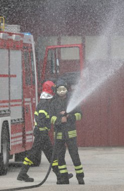 İtfaiyeciler yangın istasyonundaki tatbikat sırasında endüstriyel bir hortumla su püskürtüyorlar.