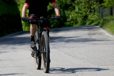 Yazın asfaltlanmış yamaç yolunda egzersiz yaparken yalnız bir bisikletçi.