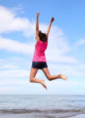 young girl while doing gymnastic exercises and jumping very high near the sea in summer