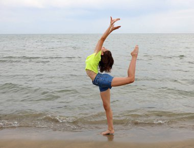 Genç, narin genç kız, deniz kıyısında ECART adı verilen arka bacağıyla sanatsal bir jimnastik egzersizi yapıyor.
