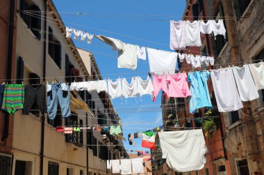 solar drying of many clothes hung with shirts, shirts, trousers in the street of the Italian city and a flag flying