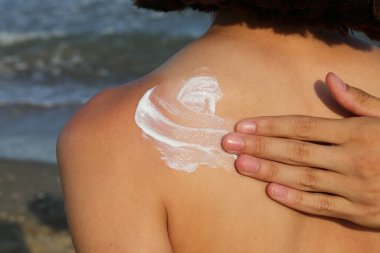 Yazın deniz kenarında genç bir kızın sırtında güneş yanıklarından korunmak için güneş kremi sürerken şefkatli bir el.