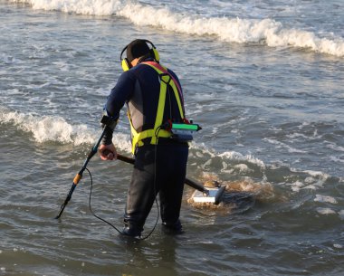 Denizin içinde dalgalı metal dedektörü olan metal maddeyi ararken su geçirmez dalış kıyafeti giymiş bir av köpeği.
