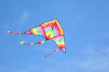 colorful kite with many colors red yellow green orange flying very high in the blue sky tied to a string