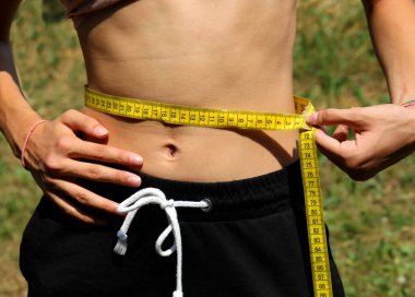 Genç, sıska bir kız, sarı bir bantla belini ölçüyor.