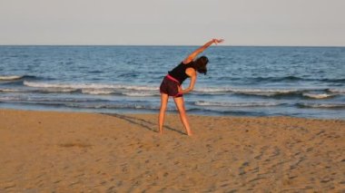 young girl does gymnastic exercises on the mat on the beach