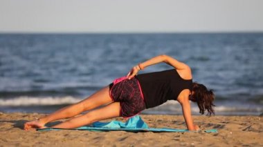 athletic girl does gymnastic exercises on the mat by the sea