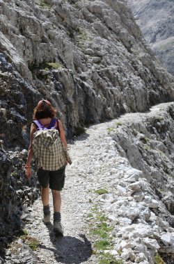 young woman walks along a stone path in the Italian Dolomites while hiking in summer
