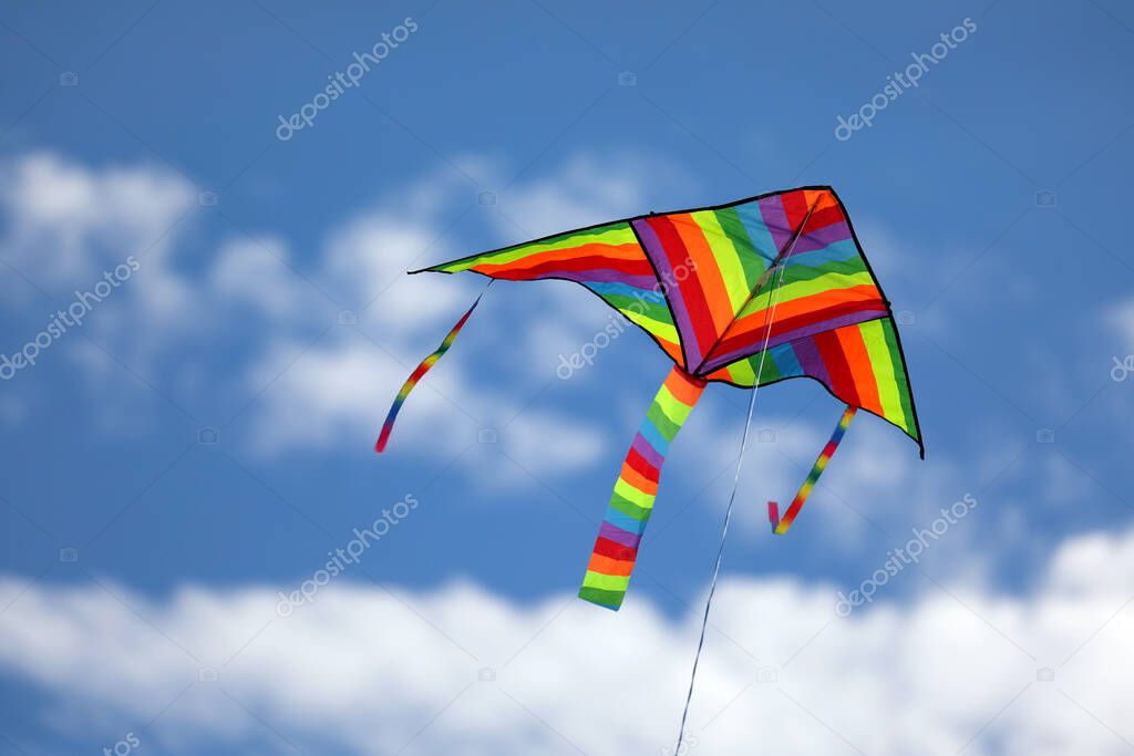 big colorful kite with rainbow colors flies in the clear summer sky