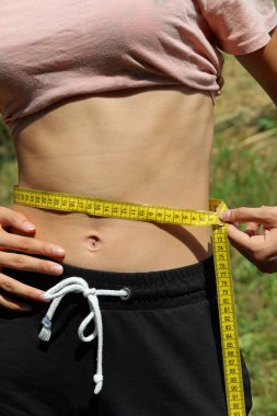 young skinny girl measuring her waist with a yellow measuring tape