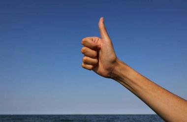 hand with thumb up indicating Ok okay perfect success the sea in the background