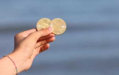 young hand holding two golden coins with the letter B indicating the cryptocurrency symbol BITCOIN