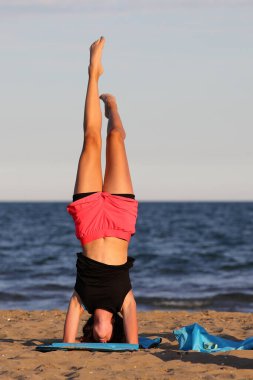 young slender athletic girl does exercises on gym mat on the beach in summer