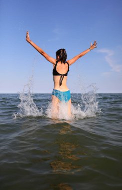 back of girl jumping out of the sea water exulting with joy and happiness