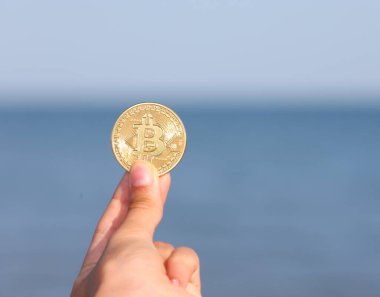 young hand holding a golden coin with the letter B indicating the symbol of the cryptocurrency BITCOIN