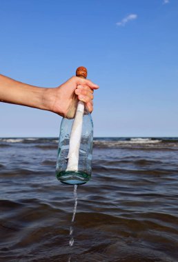 hand of the person who collects the bottle with a secret message or a treasure map in the middle of the sea