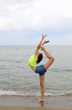 Genç ve narin bir kız yazın sahilde ECART adında sanatsal bir jimnastik egzersizi yapıyor.