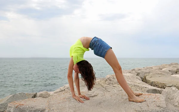 Outdoor yoga practice near the ocean. Young woman practicing Adho Mukha  Vrksasana. Yoga Handstand is an inverted asana. Beautiful asana. Strong  slim body. Yoga retreat. Copy space. Bali Stock Photo