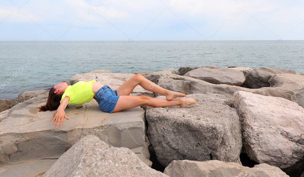 young girl sunbathes lying on the rocks by the sea in summer