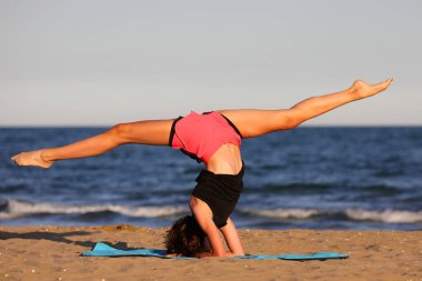 young slender athletic girl does exercises on gym mat on the beach in summer