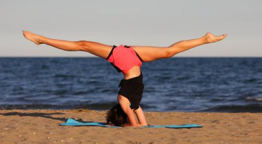 young slender athletic girl does exercises on gym mat on the beach in summer