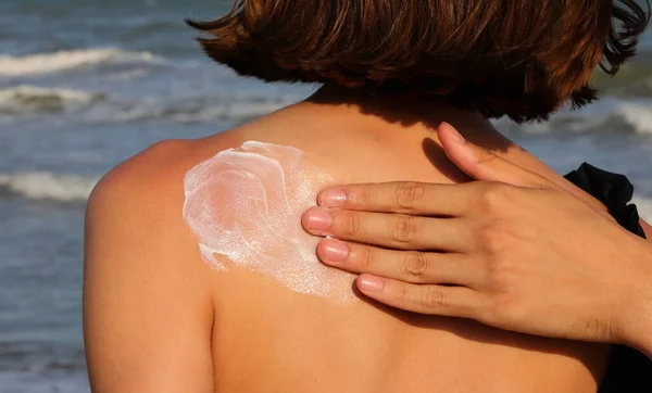 hand of man gently smearing anti sunburn lotion for protection while tanning in hte back of girl