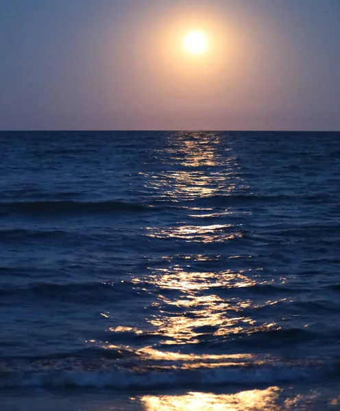 large circle of light in the evening and the reflection on the placid water of the ocean