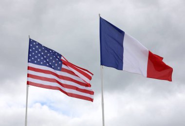 Büyük Amerikan ve Fransız bayrakları mavi gökyüzü arka planında birlikte dalgalanıyor.