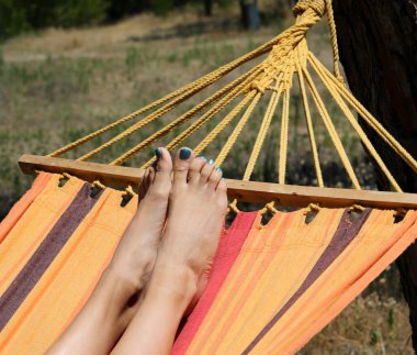 Yalınayak, renkli ojeli bir kız yazın hamakta dinleniyor.