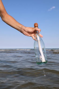 hand of the person who collects the bottle with a secret message or a treasure map in the middle of the sea