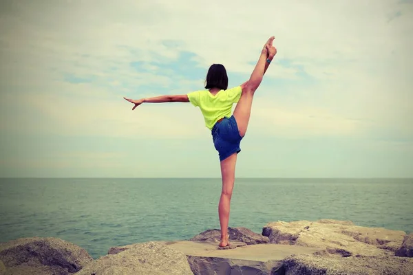 若い女の子はアンティーク調の効果で海の岩の上で体操を実行します — ストック写真