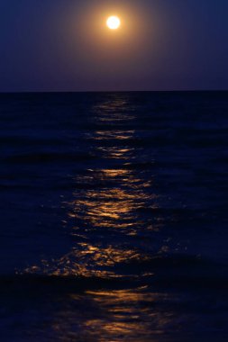 Denizden yükselen dolunay ve suyun üzerindeki ışığın yansıması.
