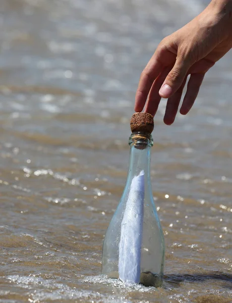 hand and secret message in the transparent glass bottle on the shore