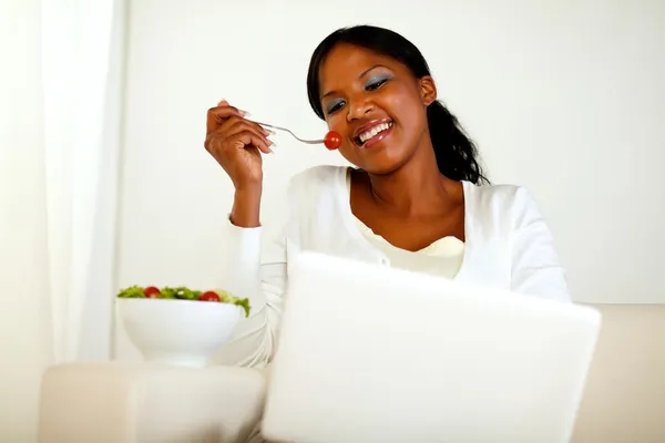 Mujer sonriente navegando por Internet comiendo una ensalada — Foto de Stock