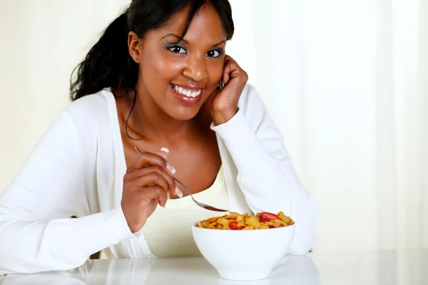 Woman looking at you and eating a bowl of cereals — Stock Photo, Image