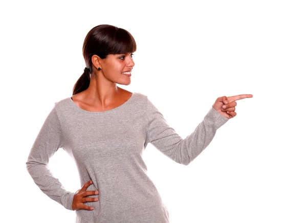 Smiling young woman on grey dress pointing left — Stock Photo, Image