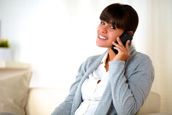 Young woman sitting on sofa speaking at cellphone — Stock Photo, Image