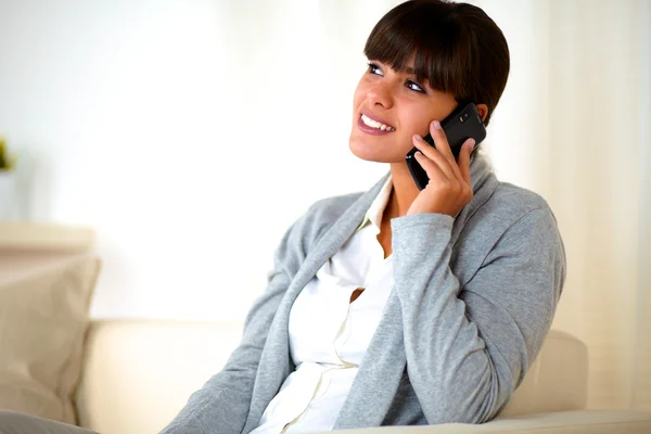 Young female sitting on sofa speaking at cellphone — Stock Photo, Image