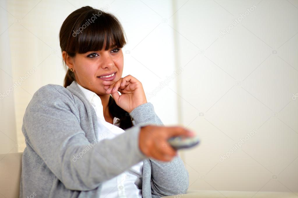 Pensive smiling young woman using a tv remote