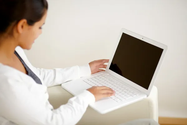 Молодая женщина сидит на диване и работает на ноутбуке — стоковое фото