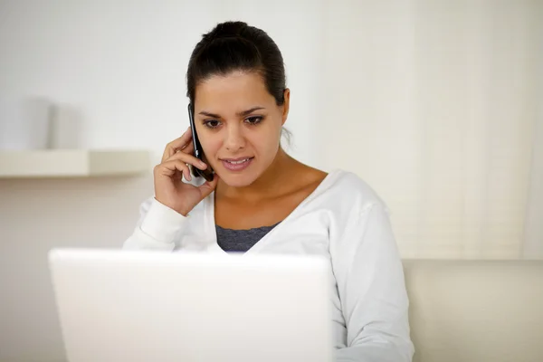 Female conversing on cellphone in front of laptop — Stock Photo, Image